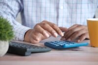 Person reviewing business costs with a calculator and paperwork